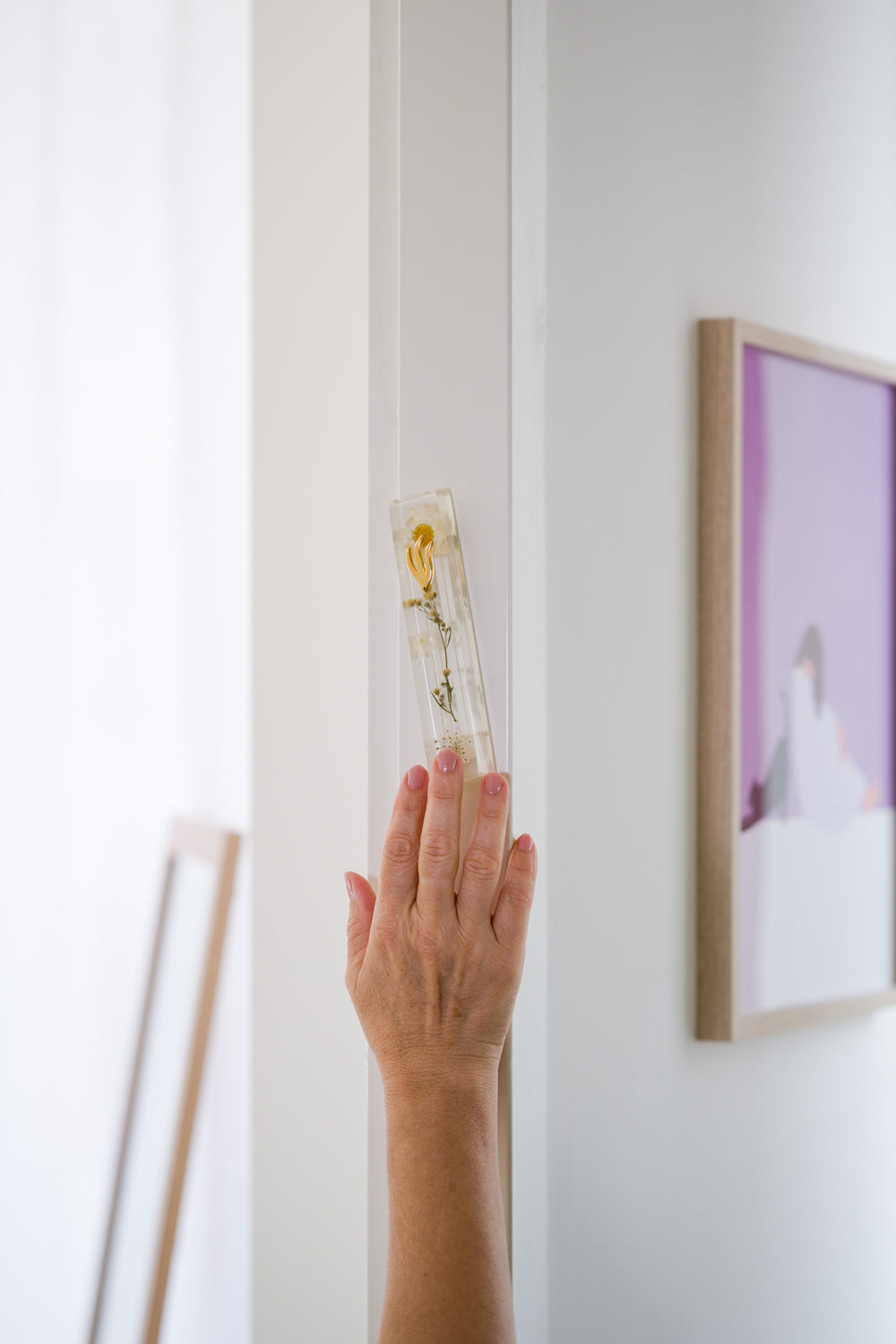 Handmade white floral mezuzah case on a doorpost, being touched and kissed by Jewish tradition.