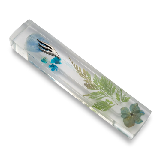 Handmade mezuzah crafted from clear resin and blue preserved flowers, featuring a silver Shin symbol on the front.