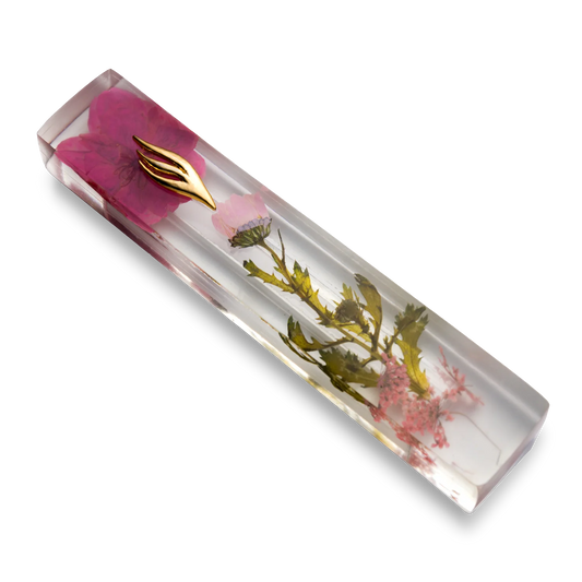 Handmade mezuzah crafted from clear resin and pink preserved flowers, featuring a golden Shin symbol on the front.