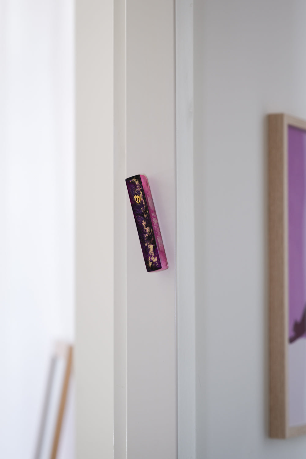 Handmade resin mezuzah case in purple colour on a doorpost, placed by the Jewish tradition.