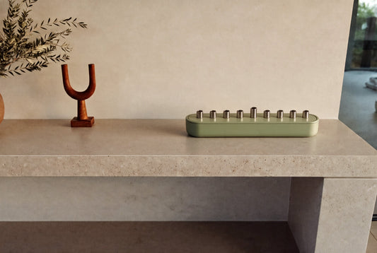 Sage green Hanukkah menorah with candle storage on a stone shelf