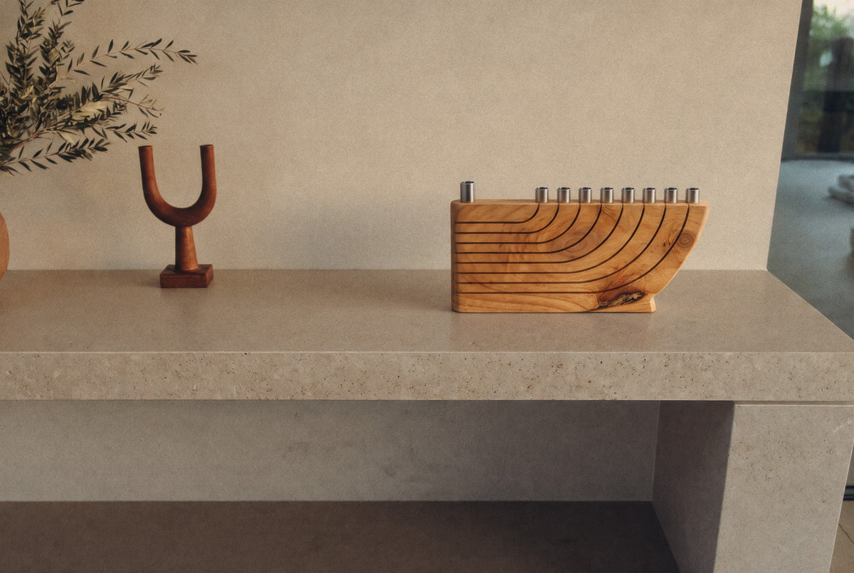 Wooden Hanukkah menorah with curved grooves and nine silver cups on a stone shelf